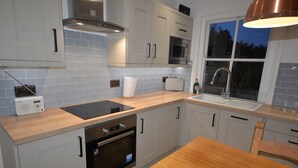 A modern kitchen with light-colored cabinets, a wooden countertop, a built-in oven, a microwave, and a window with a view of the outside. - Delightful Cottage In Sandwich - One Bedroom (Sandwich)
