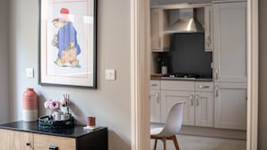 A framed picture of a cartoon character on a wall, a vase with flowers, and a black tray with a cup on a counter. - Elegant Ludlow Haven: 4Bed Ultimate Tranquility (Ludlow)
