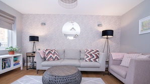 A modern living room with a grey sofa, a round ottoman, and two floor lamps. - Elegant Ludlow Haven: 4Bed Ultimate Tranquility (Ludlow)
