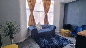 Una sala de estar con un sofá azul, una mesita auxiliar, un televisor y una planta.
