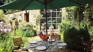 A round table set for dining with chairs, an umbrella, and a stone wall in the background. - Wonderful Picturesque Countryside Cottage (Banbury)