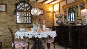 A dining area with a stone wall, wooden beams, a lace tablecloth, and striped chairs. - Wonderful Picturesque Countryside Cottage (Banbury)