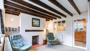 Un salon chaleureux avec deux fauteuils à motifs écossais, une cheminée, des étagères à livres et une grande fenêtre ornée d’œuvres d’art.