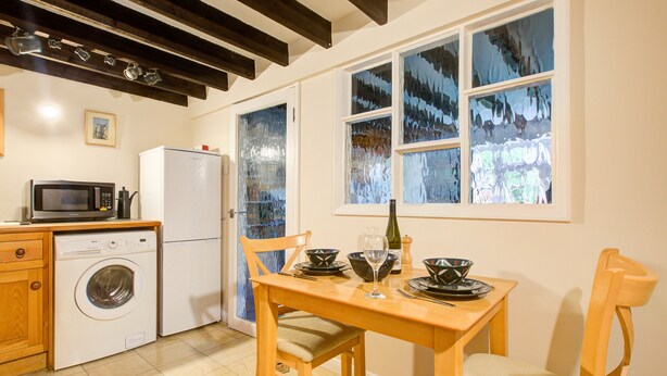 Une cuisine équipée d’un lave-linge, d’un four à micro-ondes et d’un réfrigérateur. On y trouve une table à manger avec des chaises, ainsi qu’une fenêtre avec du verre dépoli.