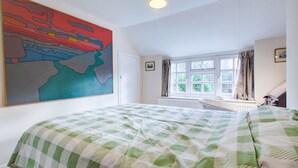 Une chambre avec un grand lit, une fenêtre avec des rideaux, un radiateur et une peinture abstraite aux couleurs vives accrochée au mur.