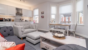 A modern kitchen with white cabinets, a grey sofa, and a dining area with a table and chairs. - Little Boat: A Modern Beachside Flat (Bournemouth)