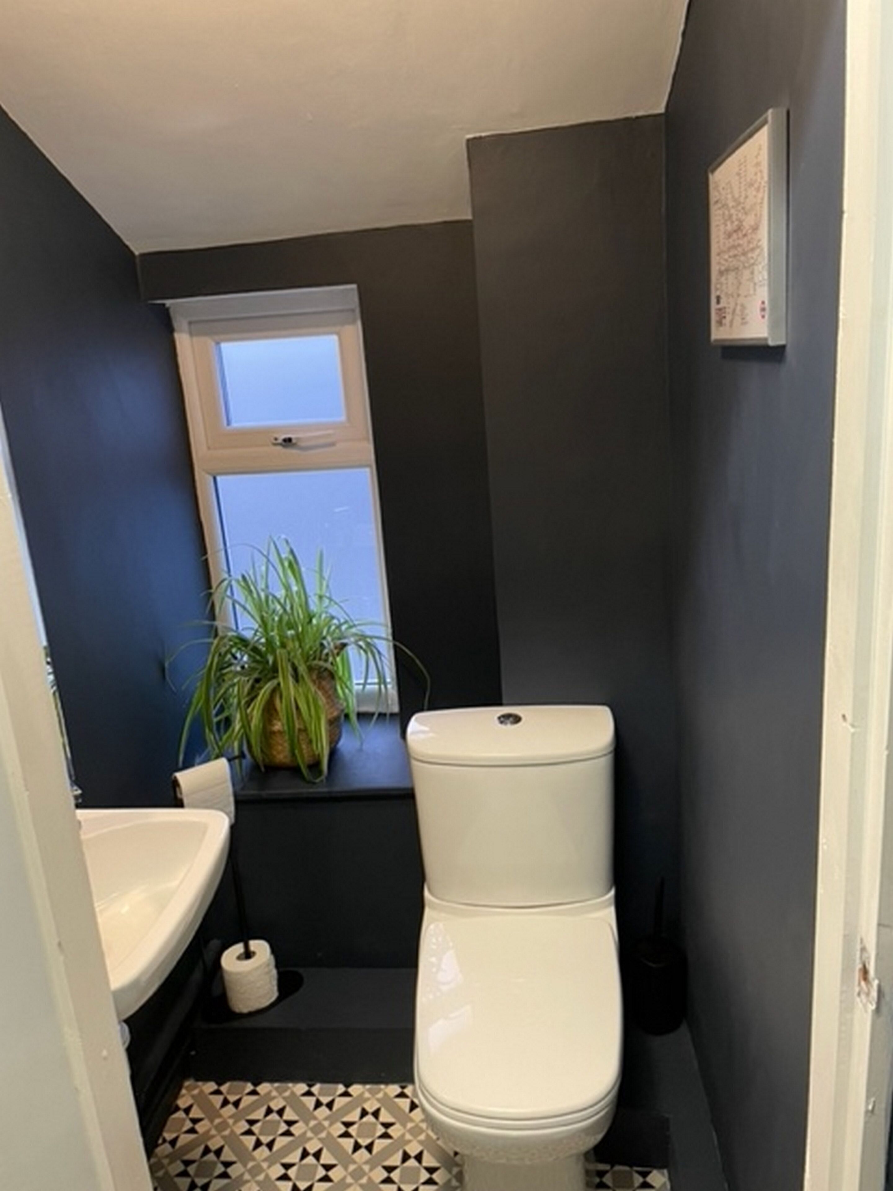 A small, dark-colored bathroom with a toilet, sink, and window.
