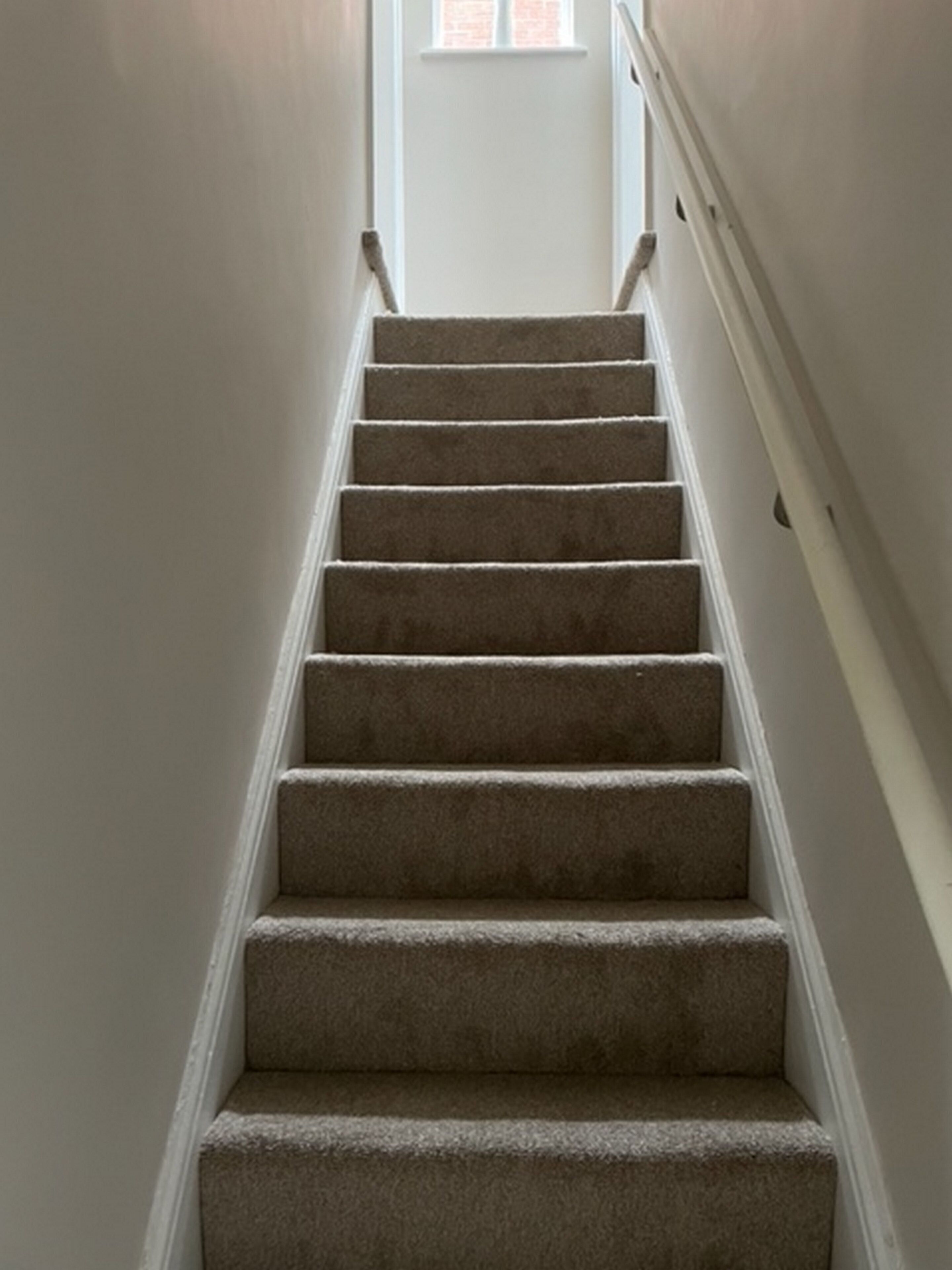 A carpeted staircase with white walls and a door at the top.