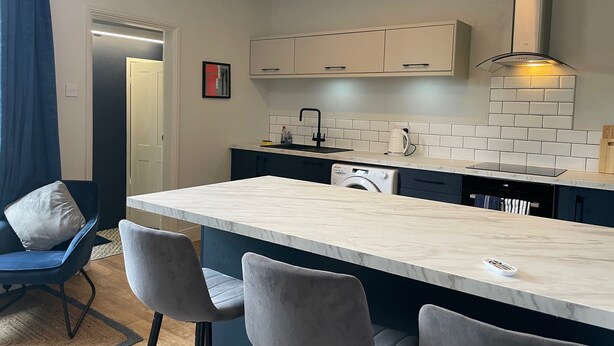A modern kitchen with a marble countertop, built-in appliances, and a small island with bar stools.