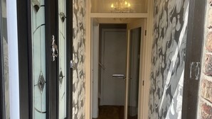 A hallway with a wooden floor, a black door with glass panels, and a wall with a floral pattern.