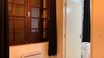 Una camera d'albergo con un letto, un termosifone, una finestra con tende e una porta che dà su un'altra stanza.
