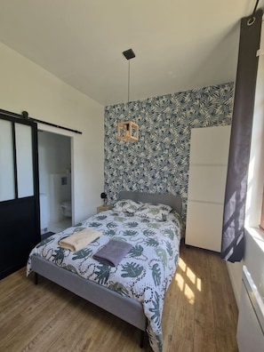 Une chambre à coucher comprenant un lit, une armoire, un luminaire suspendu et une fenêtre avec des rideaux.