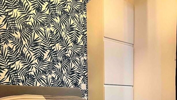 A hotel room with a bed, a patterned wall, and a wardrobe.