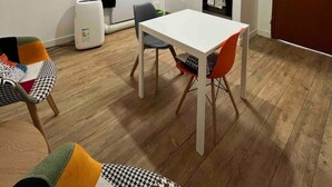 A compact kitchen with white cabinets, a red backsplash, and a dining area with a white table and two chairs.