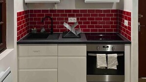 A compact kitchen with white cabinets, a red-tiled backsplash, a black countertop, a stainless steel sink, and a built-in oven.