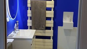 A bathroom with a blue wall, a white sink, a mirror, and a towel rack. - Studio on Metro Line B at La Vache (Toulouse)
