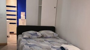 A bedroom with a bed, a blue chair, a wardrobe, and a shelving unit. - Studio on Metro Line B at La Vache (Toulouse)