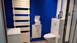 A modern bathroom with a blue accent wall, a white toilet, a glass shower enclosure, and a white sink. - Studio on Metro Line B at La Vache (Toulouse)