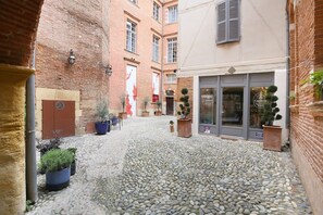 Uma ruela estreita com calçada de pedra, plantas em vasos e um edifício com uma placa indicando 'Capitole'.