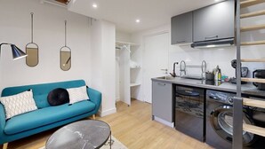 A compact living space with a kitchenette, a sofa, a washing machine, and a ceiling with exposed beams.