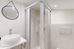 Een badkamer met een witte wastafel, een douche met glazen wanden en een spiegel aan de muur.
