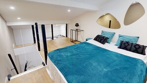A modern bedroom with a skylight, a bed with teal bedding, and a small side table.