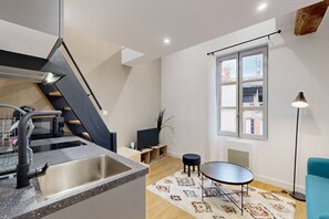 Una cocina moderna con pileta integrada, un comedor con mesa redonda y una escalera que sube a un nivel superior.