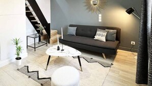 A modern living room with a sofa, coffee table, ottoman, and a staircase leading to an upper level.