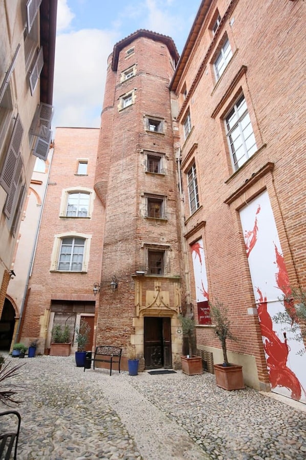 Un callejón estrecho con un edificio alto de ladrillo, plantas en macetas y un banco.