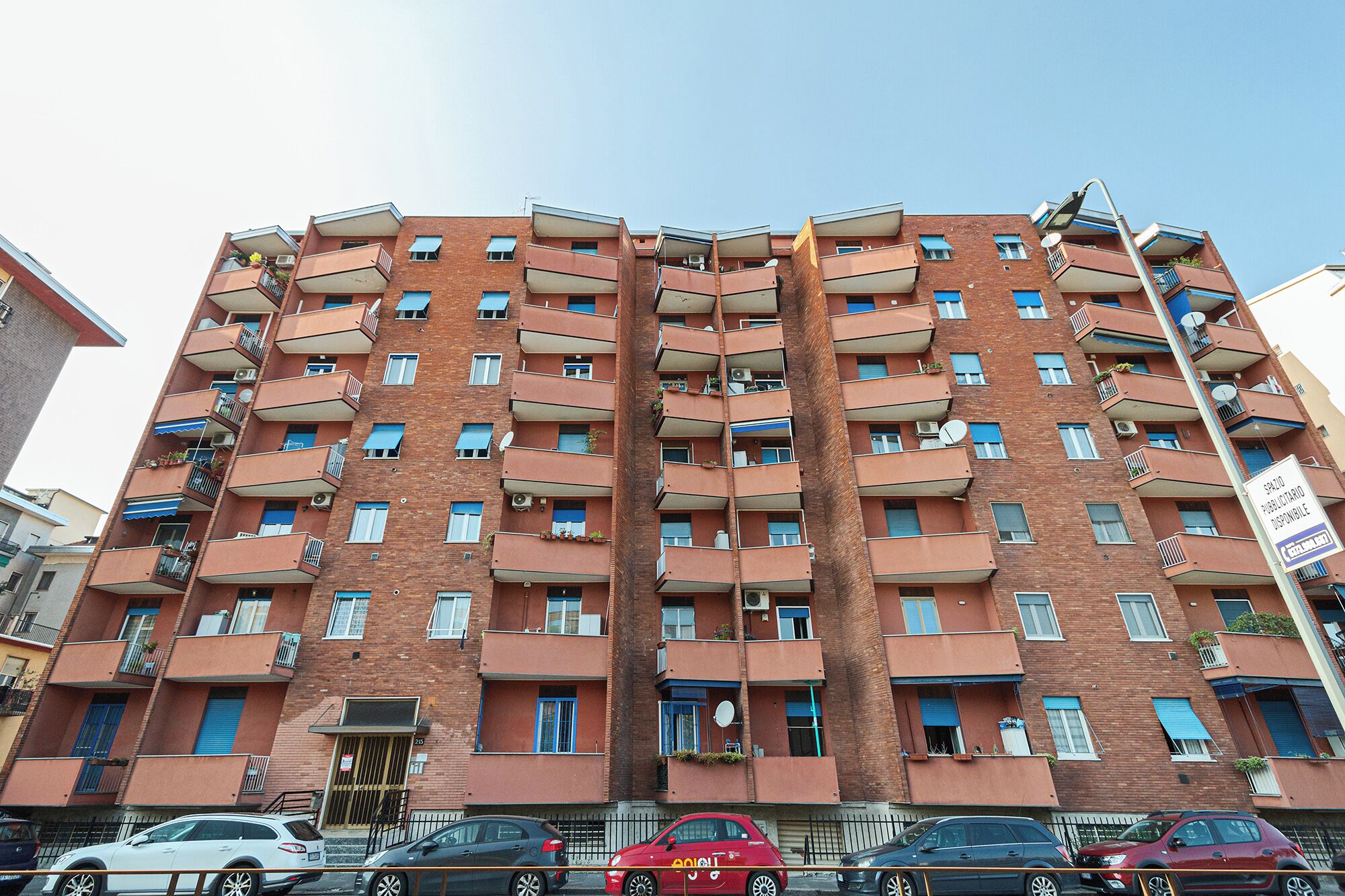 A multi-story residential building with balconies, a visible entrance, and a street view.