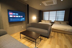 A modern hotel room with a sofa, a bed, a wooden floor, and a wall-mounted TV displaying various streaming services. - MUSASHI Condo Kanazawa (Kanazawa)