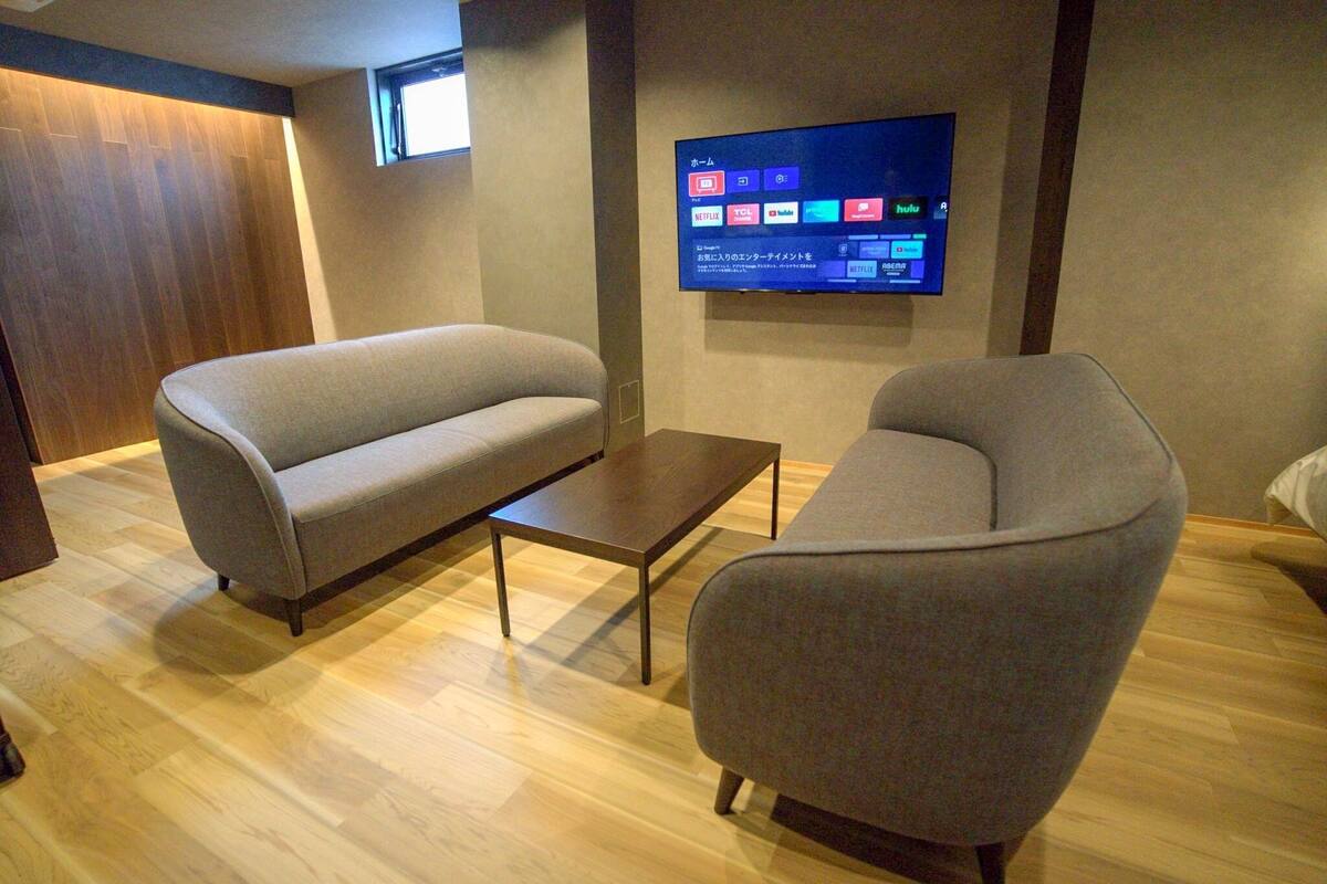 Ett modernt vardagsrum med en soffa, fåtölj och soffbord. En platt-TV är monterad på väggen och visar olika streamingtjänster.
