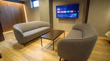 Een moderne woonkamer met een bank, fauteuil en salontafel. Een flatscreen televisie aan de muur toont verschillende streamingdiensten.