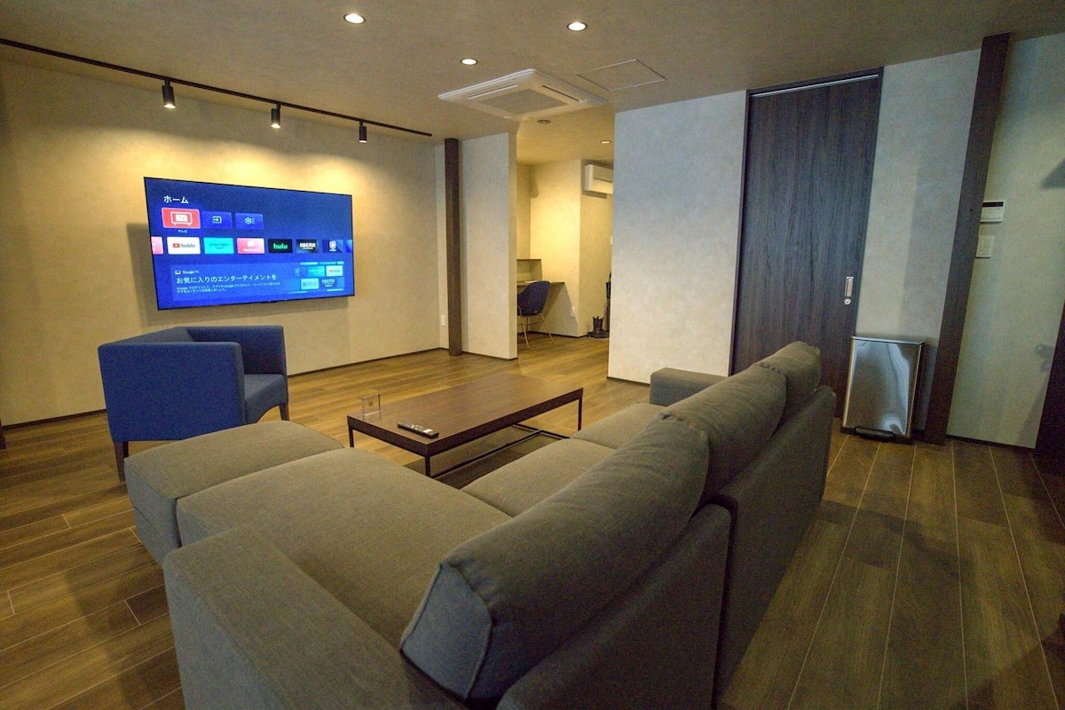 Ett modernt vardagsrum med en stor platt-TV som är monterad på väggen, en soffa, ett soffbord och en liten fåtölj.