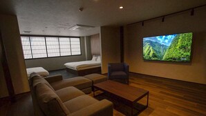 A modern hotel room with a large flat-screen TV, a sofa, a bed, and a wooden coffee table. - MUSASHI Condo Kanazawa (Kanazawa)
