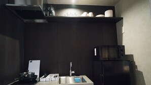 A modern kitchen with a built-in microwave, a sink, and a countertop with a cutting board and utensils. - MUSASHI Condo Kanazawa (Kanazawa)
