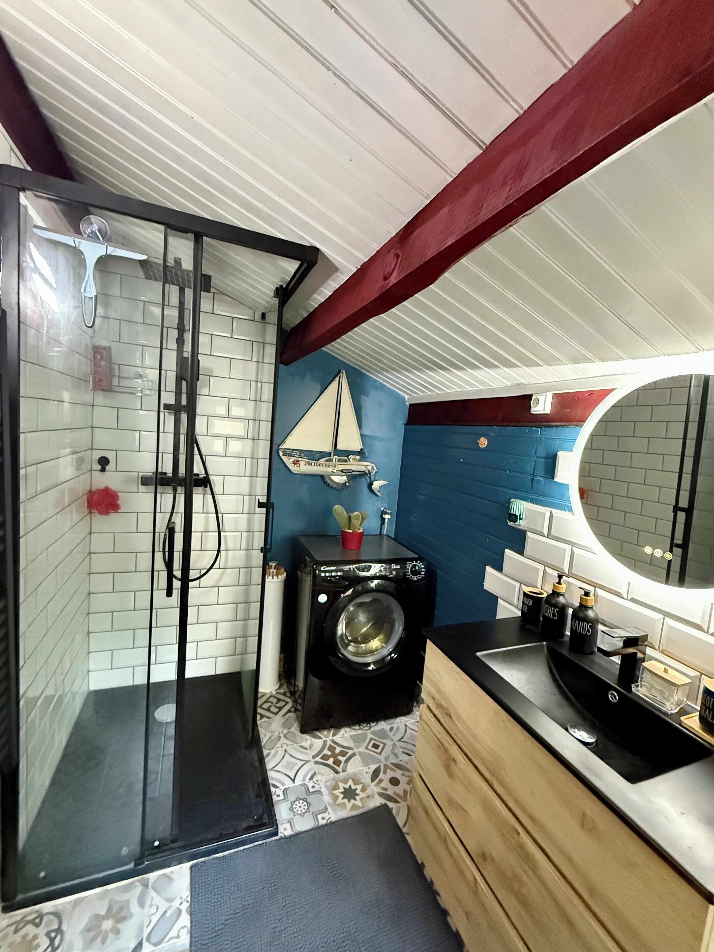 A compact bathroom with a glass shower enclosure, a washing machine, and a sink with a mirror.