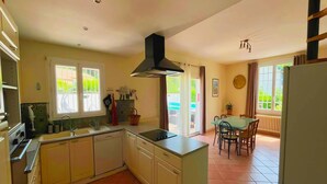 Une cuisine dotée d’un îlot central, un coin repas avec une table et des chaises, et une vue sur l’extérieur grâce à une porte coulissante.