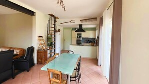 Un espace repas avec une table et des chaises en verre, une cuisine à l’arrière-plan et un escalier menant à un autre niveau.