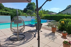 Zona de piscina con una silla de metal, una manguera y plantas en macetas.