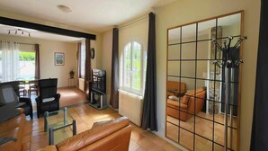 Un salon spacieux avec un canapé, des fauteuils, un téléviseur et un grand miroir.