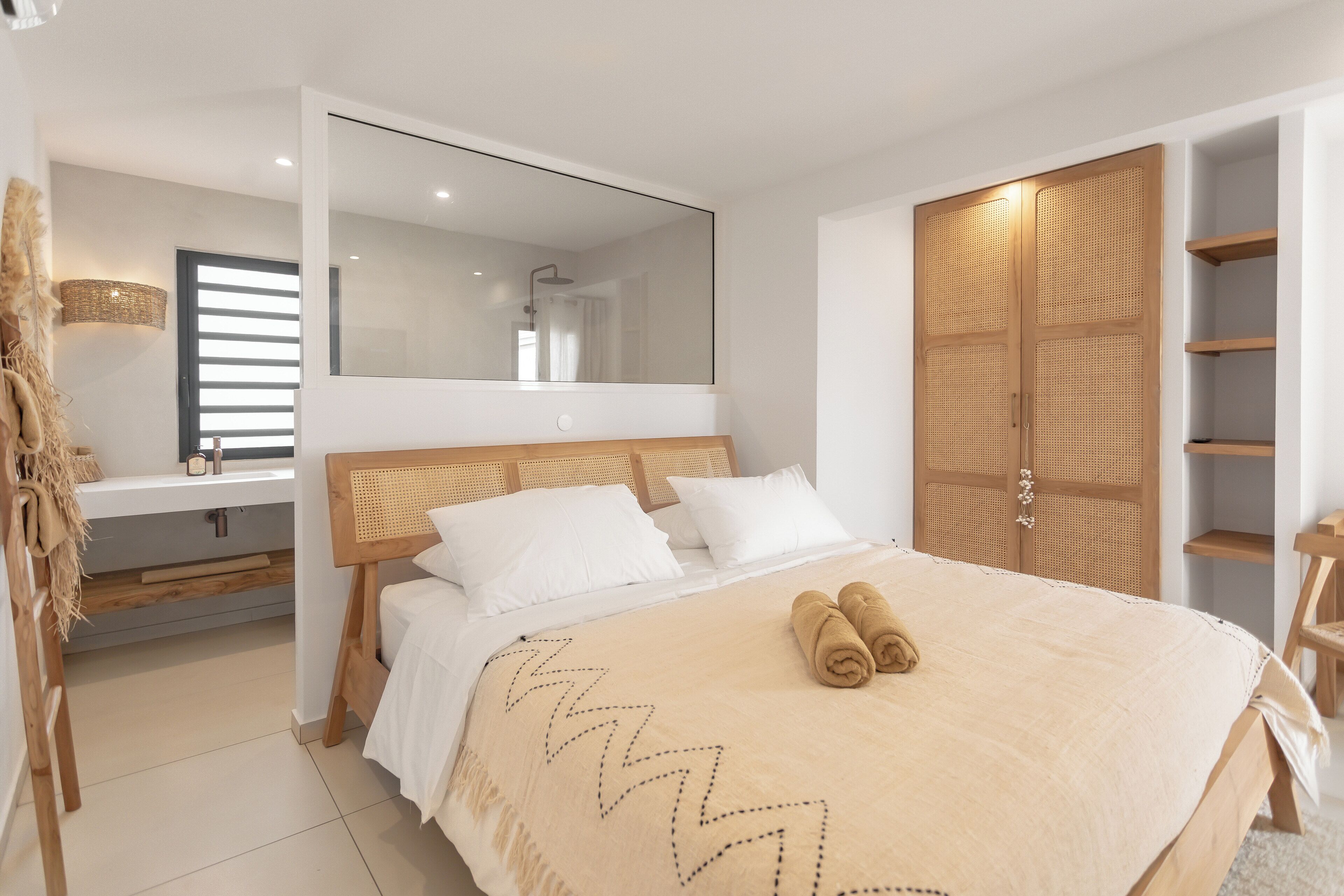 Un dormitorio moderno con una cama grande, un armario de madera, un espejo y un baño con lavabo y toallero.