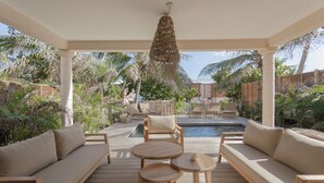 A covered outdoor area with a pool, wooden furniture, and tropical plants. - Villa Aroa (Collectivité de Saint-Martin)
