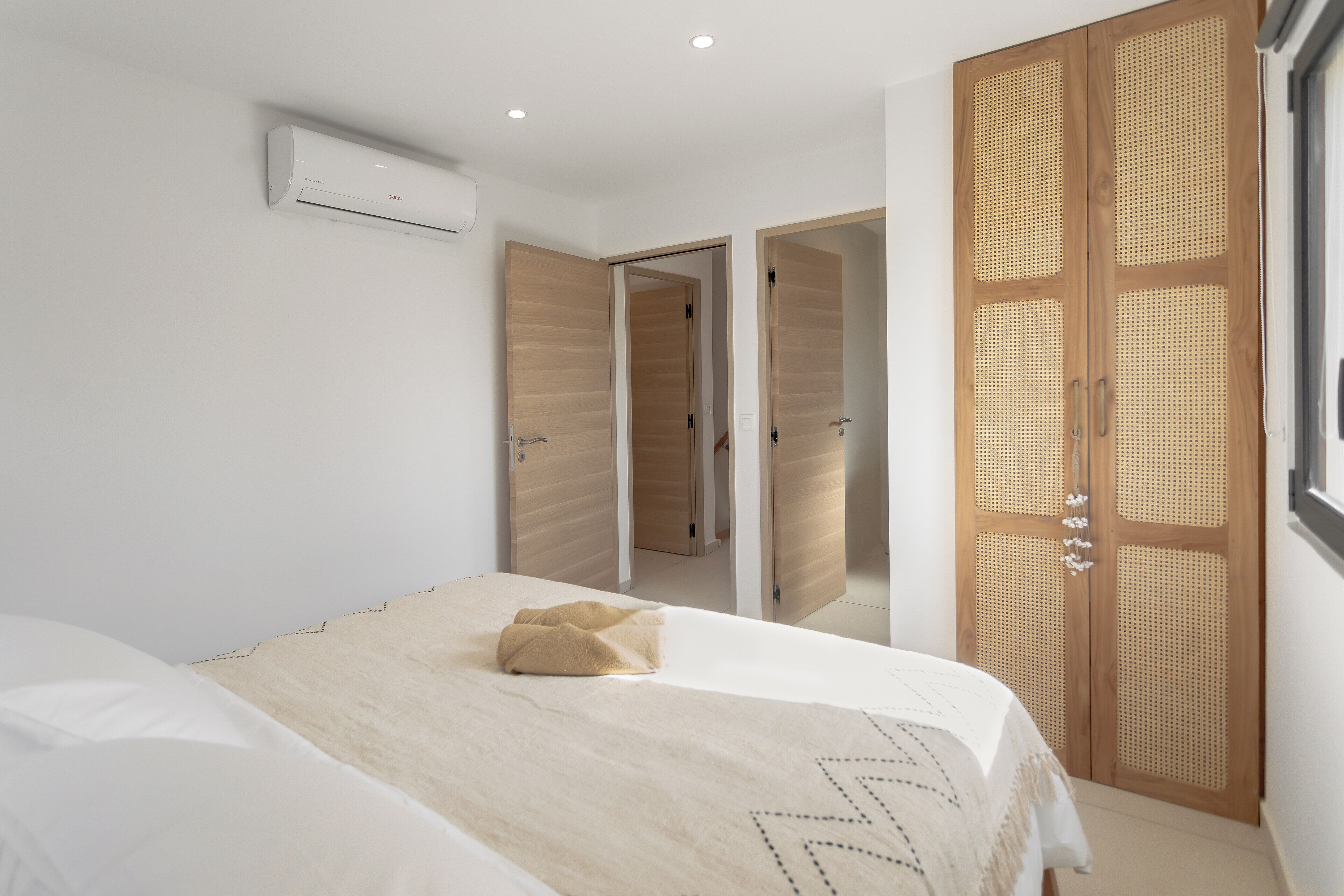 Een slaapkamer met een bed, een witte airconditioner en een houten garderobe met geweven details.