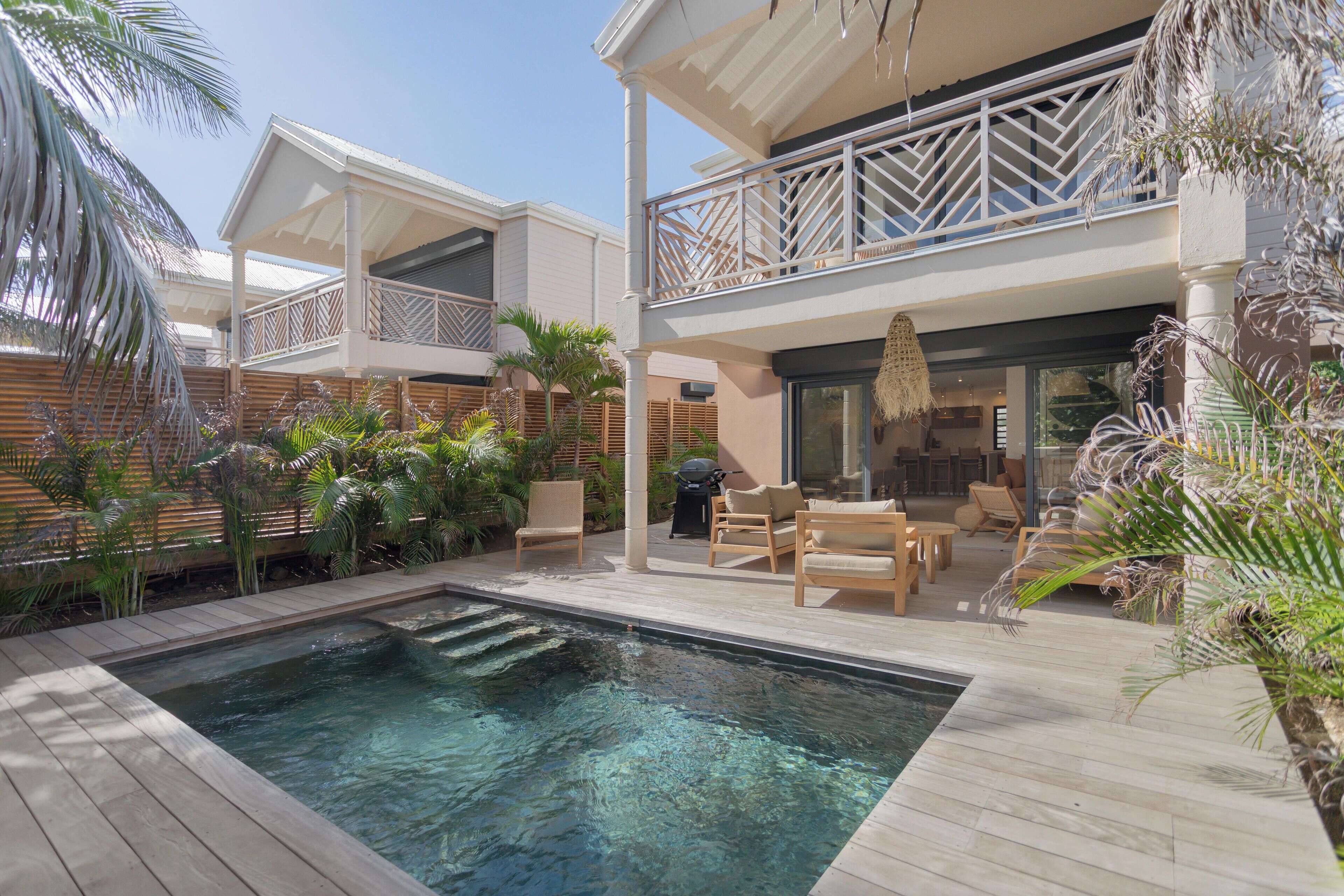 A pool area with wooden decking, lounge chairs, and a covered seating area with a view of the pool.