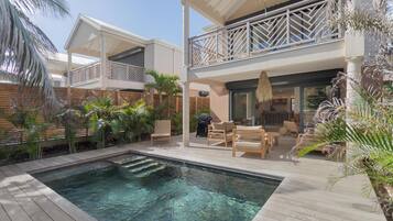 A pool area with wooden decking, lounge chairs, and a covered seating area with a view of the pool.