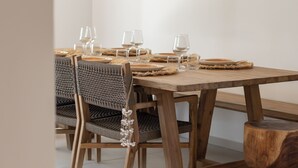 A dining area with a wooden table, woven chairs, and a hanging light fixture. - Villa Aroa (Collectivité de Saint-Martin)