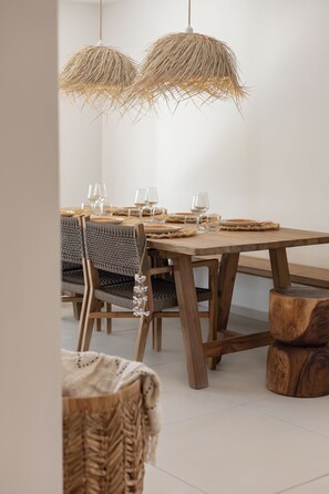 A dining area with a wooden table, woven chairs, and a hanging light fixture.