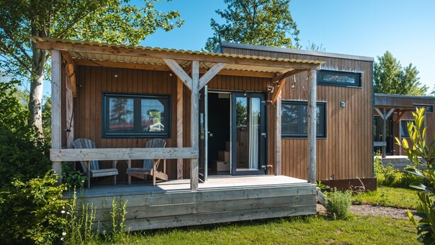 A modern cabin with a wooden deck, large sliding glass doors, and a covered porch area. - Group accommodation for 40 guests (Scherpenzeel (FR))