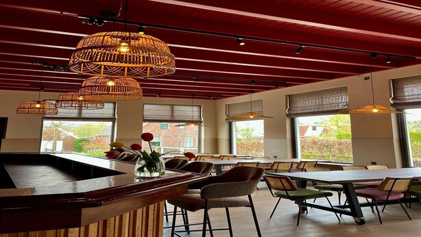 A restaurant with a wooden bar, multiple tables, wicker hanging lights, and large windows with a view of the outside. - Luxury Group Retreat in Nature (Scherpenzeel (FR))